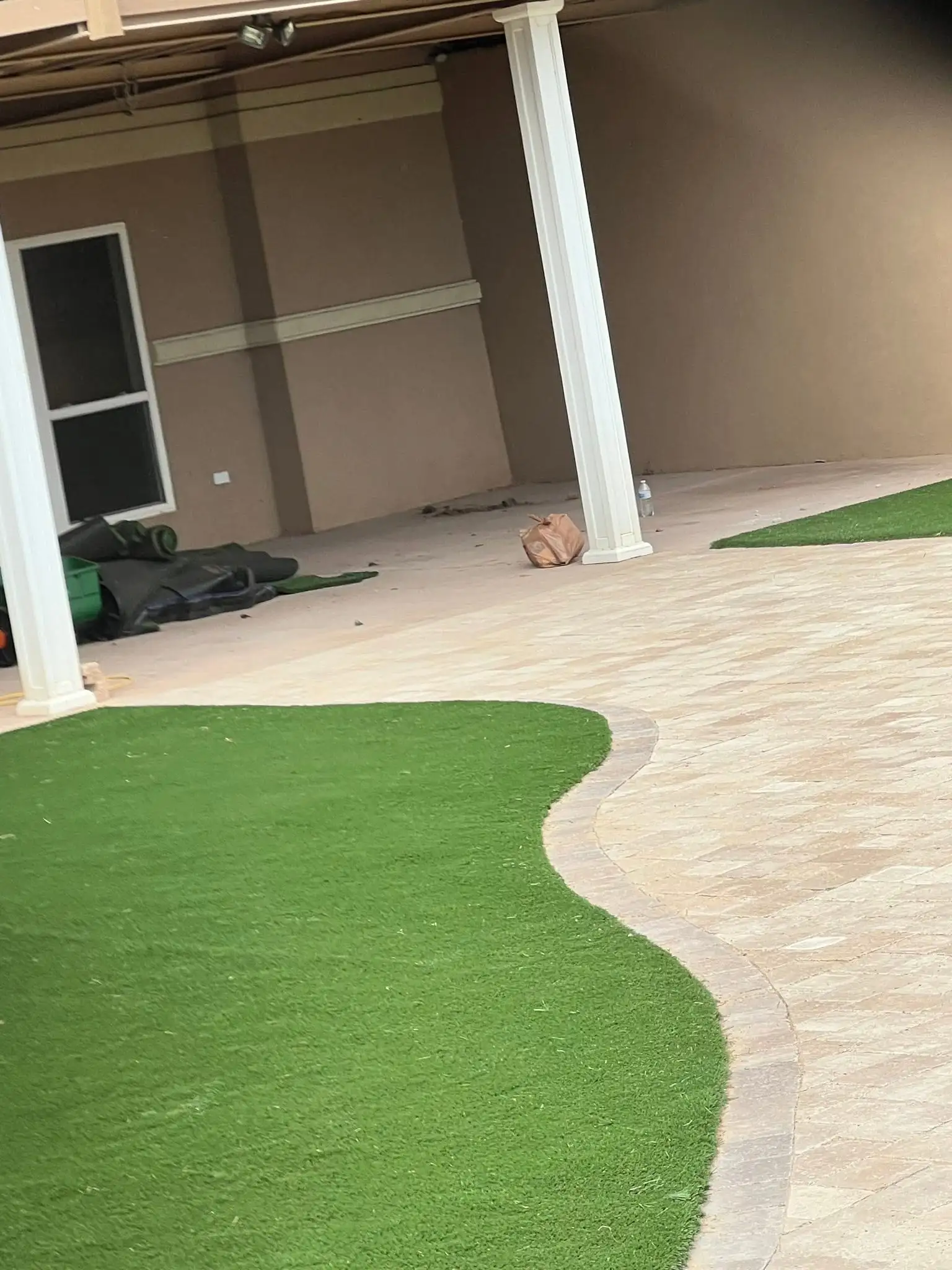 Paver patio with a curving paver border and a curved section of artificial turf beside a covered porch with white columns