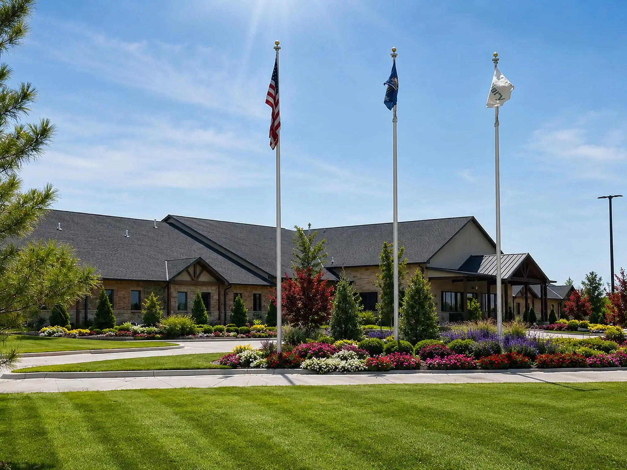Commercial building with three flagpoles, colorful flower beds, ornamental trees and a striped lawn in front