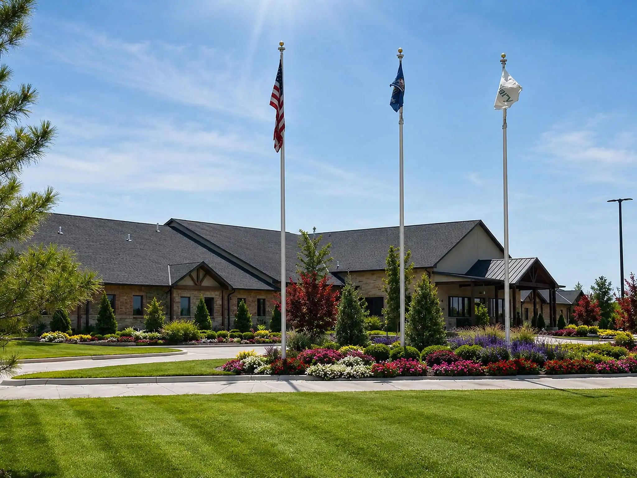 Commercial building with three flagpoles, colorful flower beds, ornamental trees and a striped lawn in front