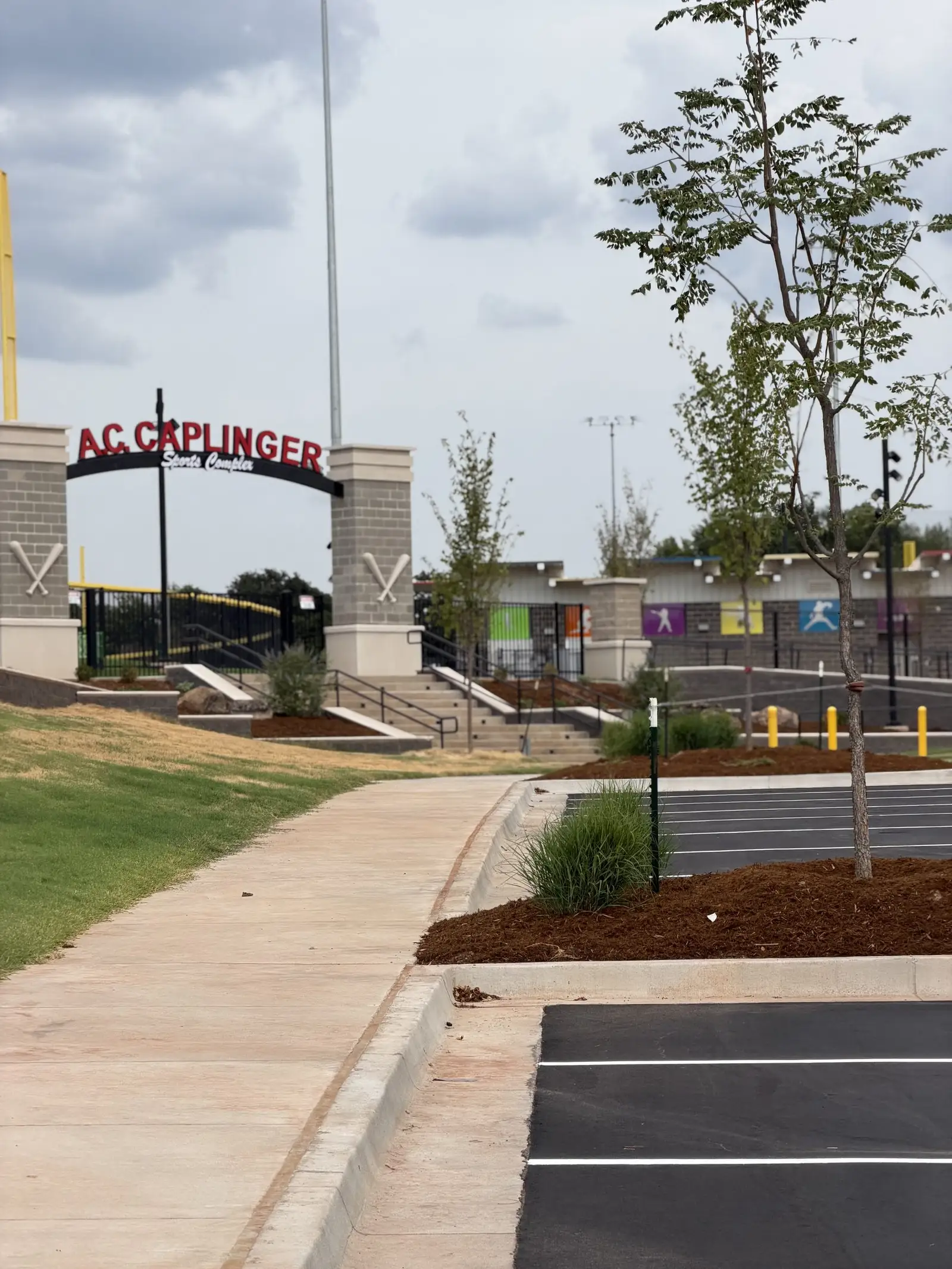 Entrance arch reading A.C. Caplinger with stone columns, behind a new mulched planting bed of ornamental grasses and a young staked tree