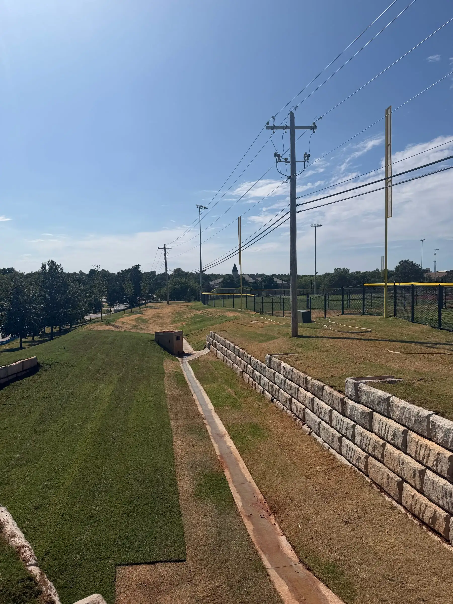 New sod on a long slope beside a stacked block retaining wall and a concrete drainage swale