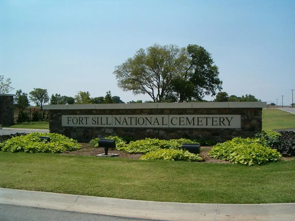 Fort Sill National Cemetery stone entrance sign above a planted bed on a mowed green lawn