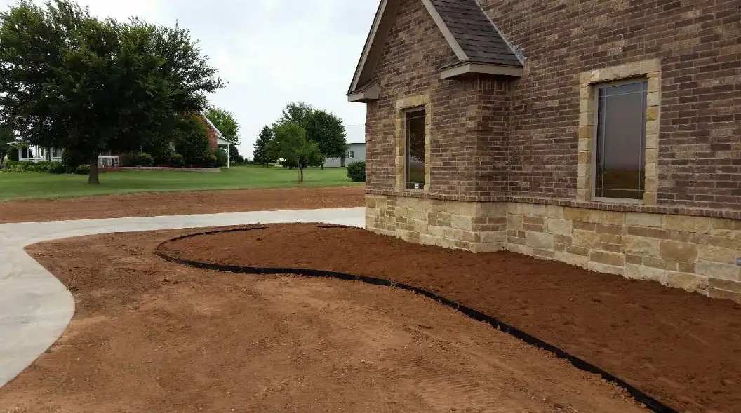 Graded front yard with a curved bed edge beside a stone home