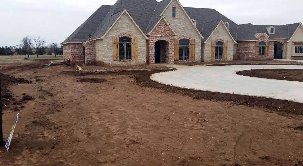 Large stone home with a curved drive and graded yard ready for planting