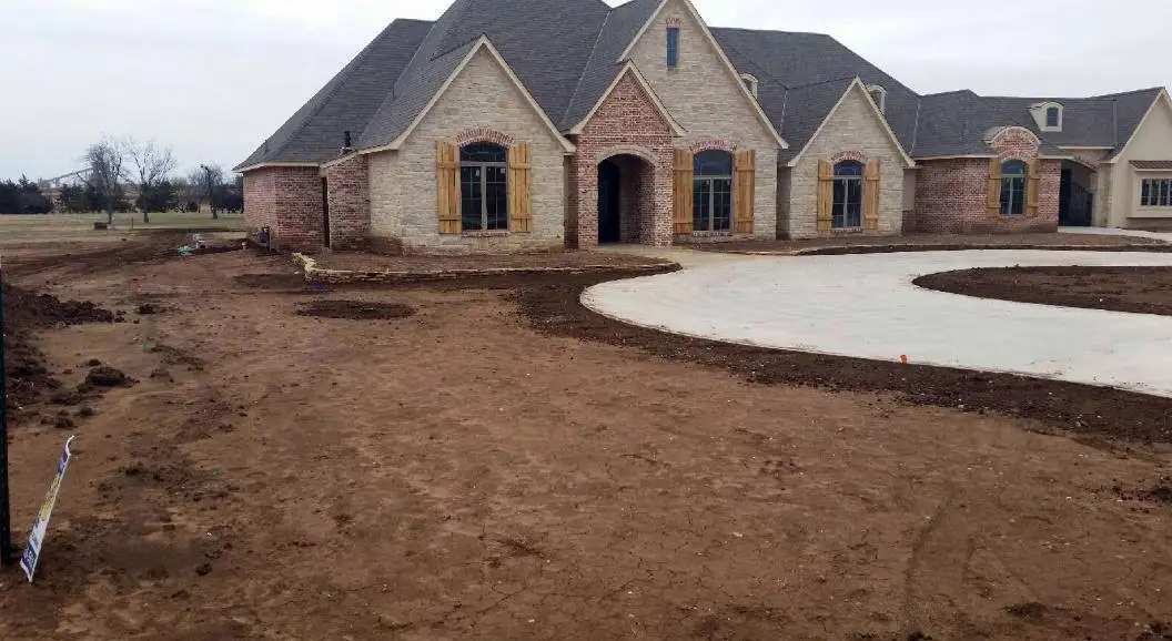 Large stone home with a curved drive and graded yard ready for planting
