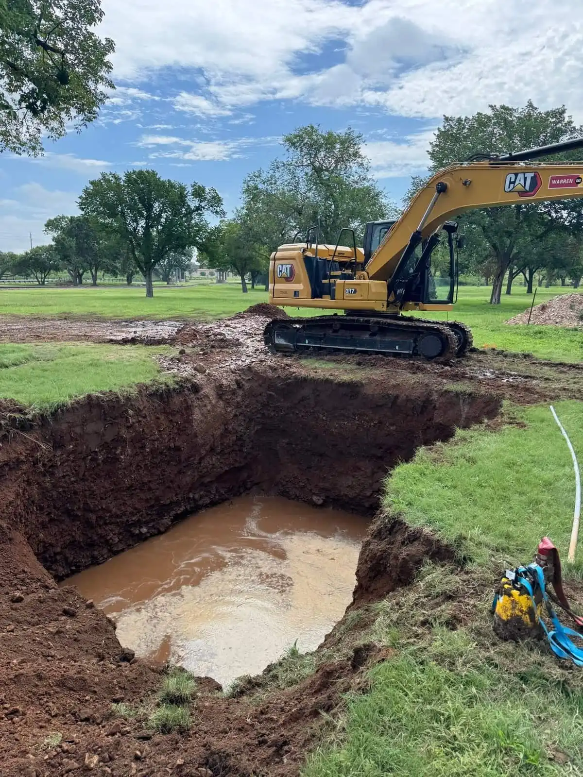 Excavator beside a deep excavation filled with water on a grass site