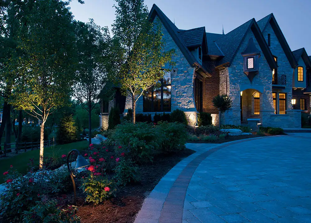 Example of landscape lighting on a stone home, driveway and trees at night