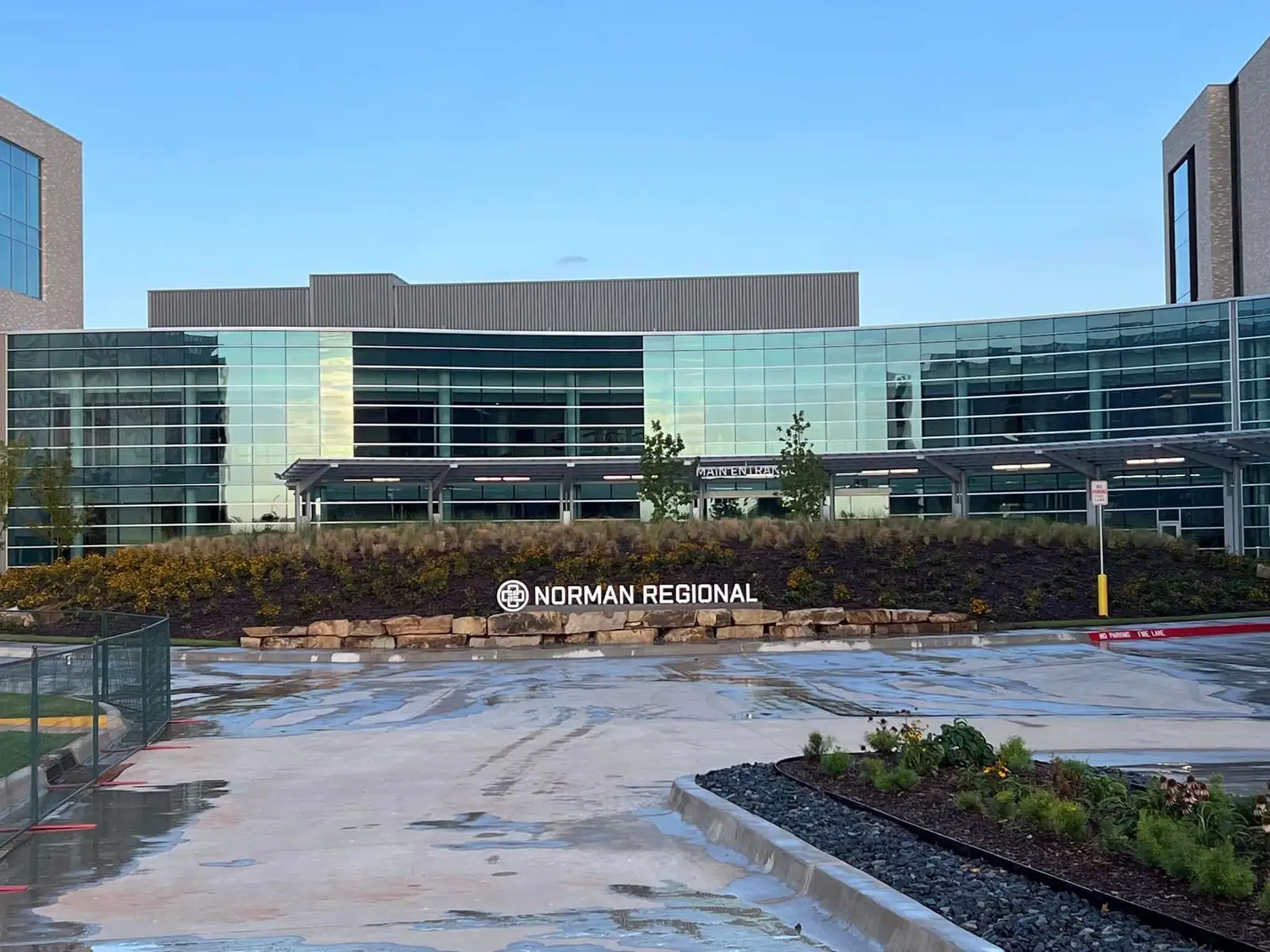Landscaped hillside with boulder retaining wall, mulch beds and flowering plants at a medical campus entrance in Norman, Oklahoma
