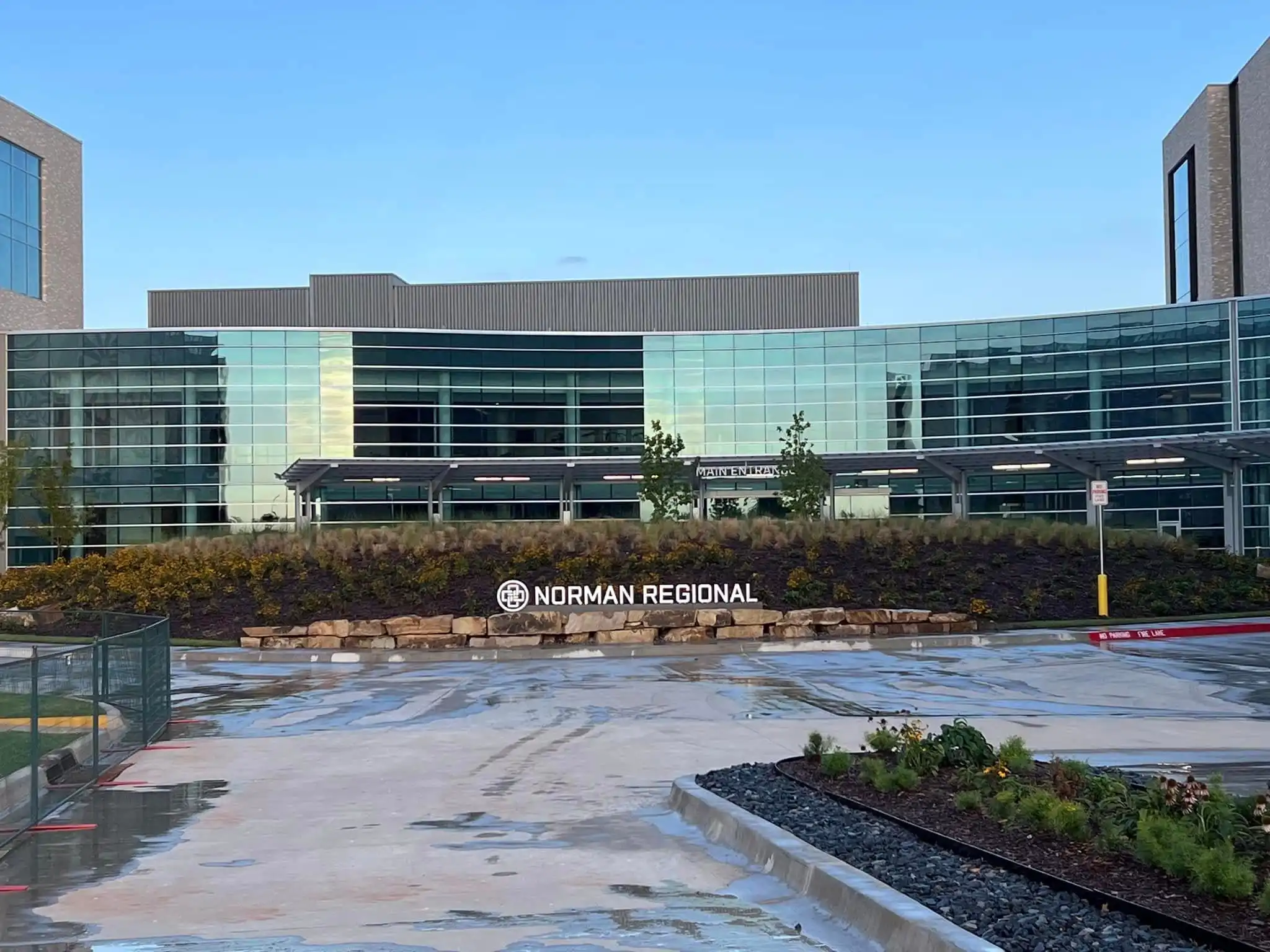 Landscaped hillside with boulder retaining wall, mulch beds and flowering plants at a medical campus entrance in Norman, Oklahoma