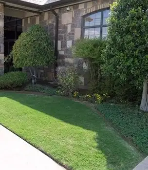 Stone-front building with a green lawn, rounded shrubs and planted beds along the walls