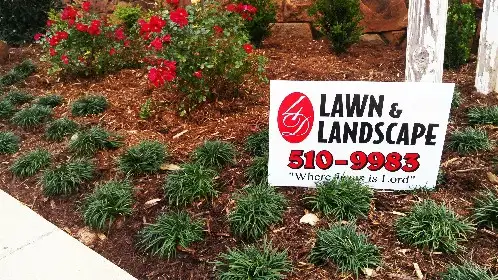 Red flowers and groundcover with a 4-D Lawn and Landscape yard sign that reads Where Jesus is Lord